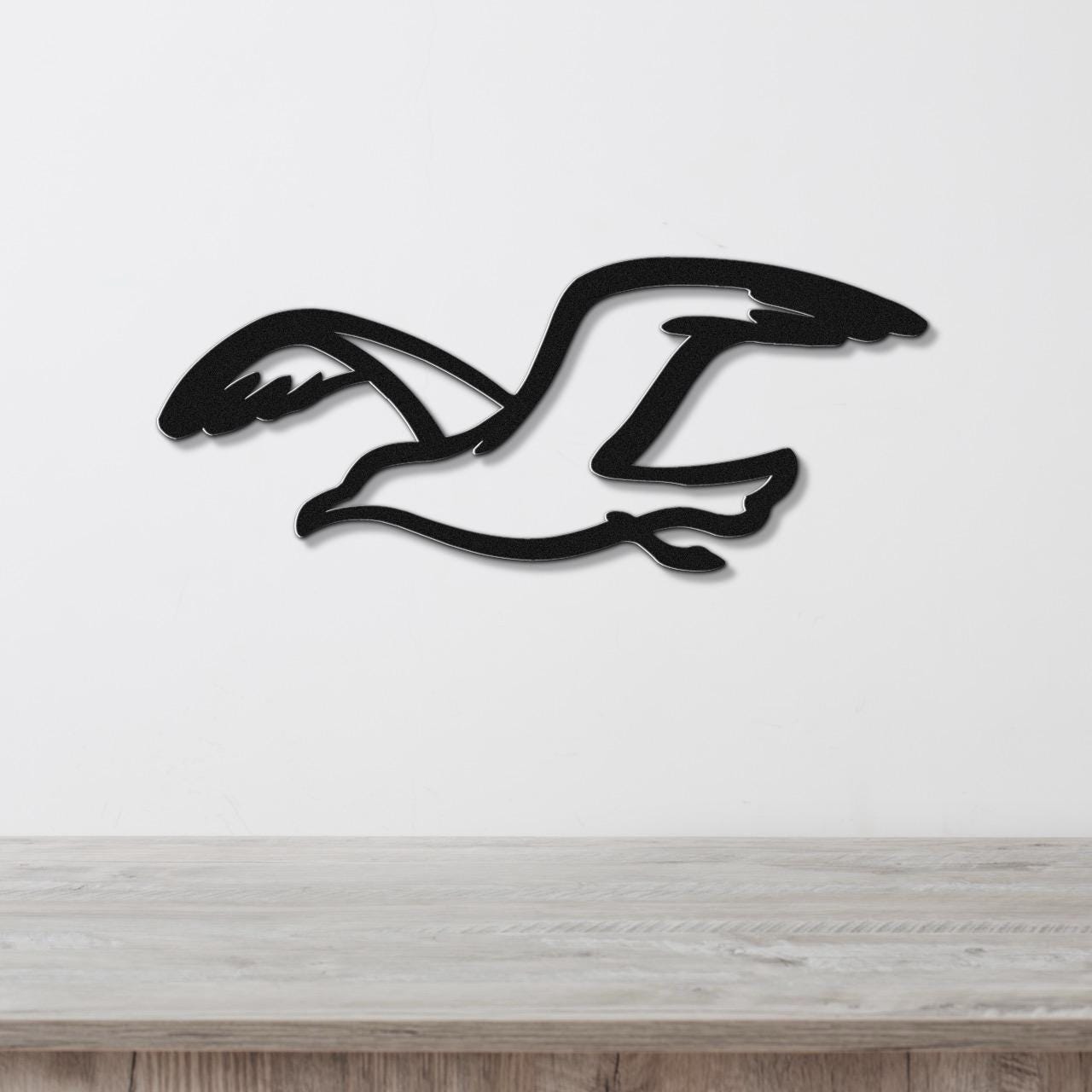 Black metal seagull wall art with a cutout silhouette design, mounted on a white wall above a light wood surface.