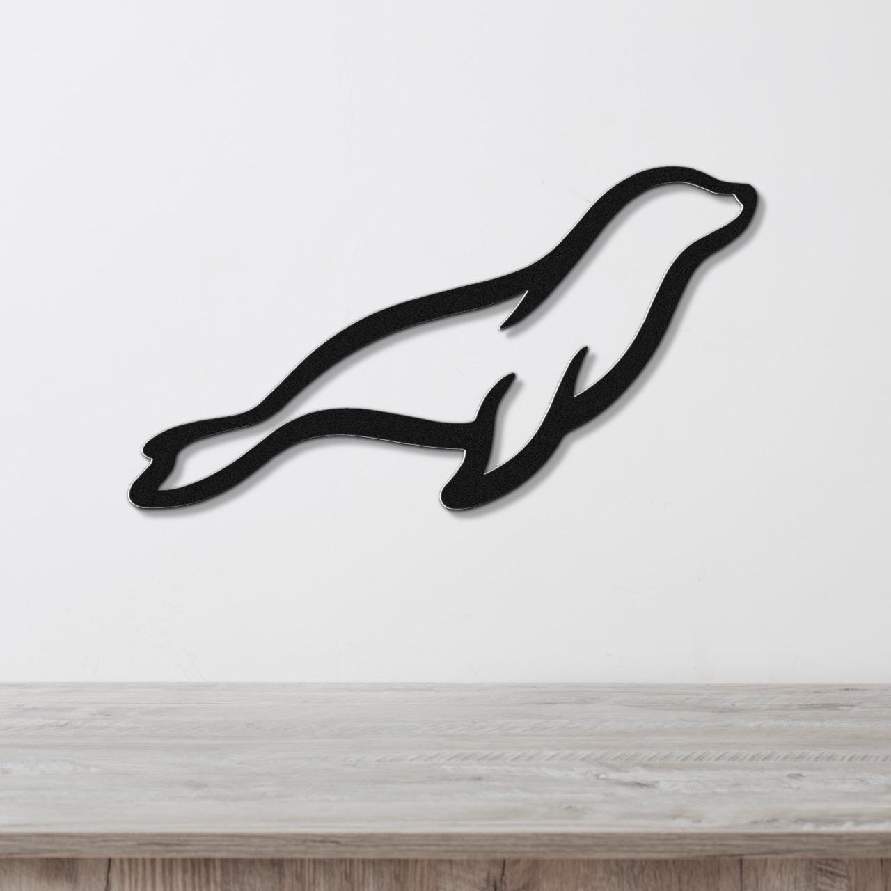 Black metal sea lion wall art with a sleek silhouette design, mounted on a white wall above a light wood surface.