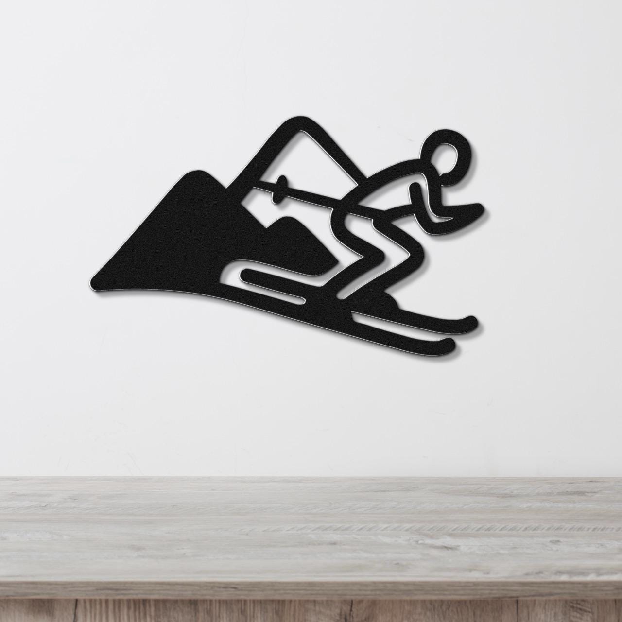 Black metal wall art featuring a skier silhouette in motion with mountain cutout, mounted on a white wall above a wooden surface.