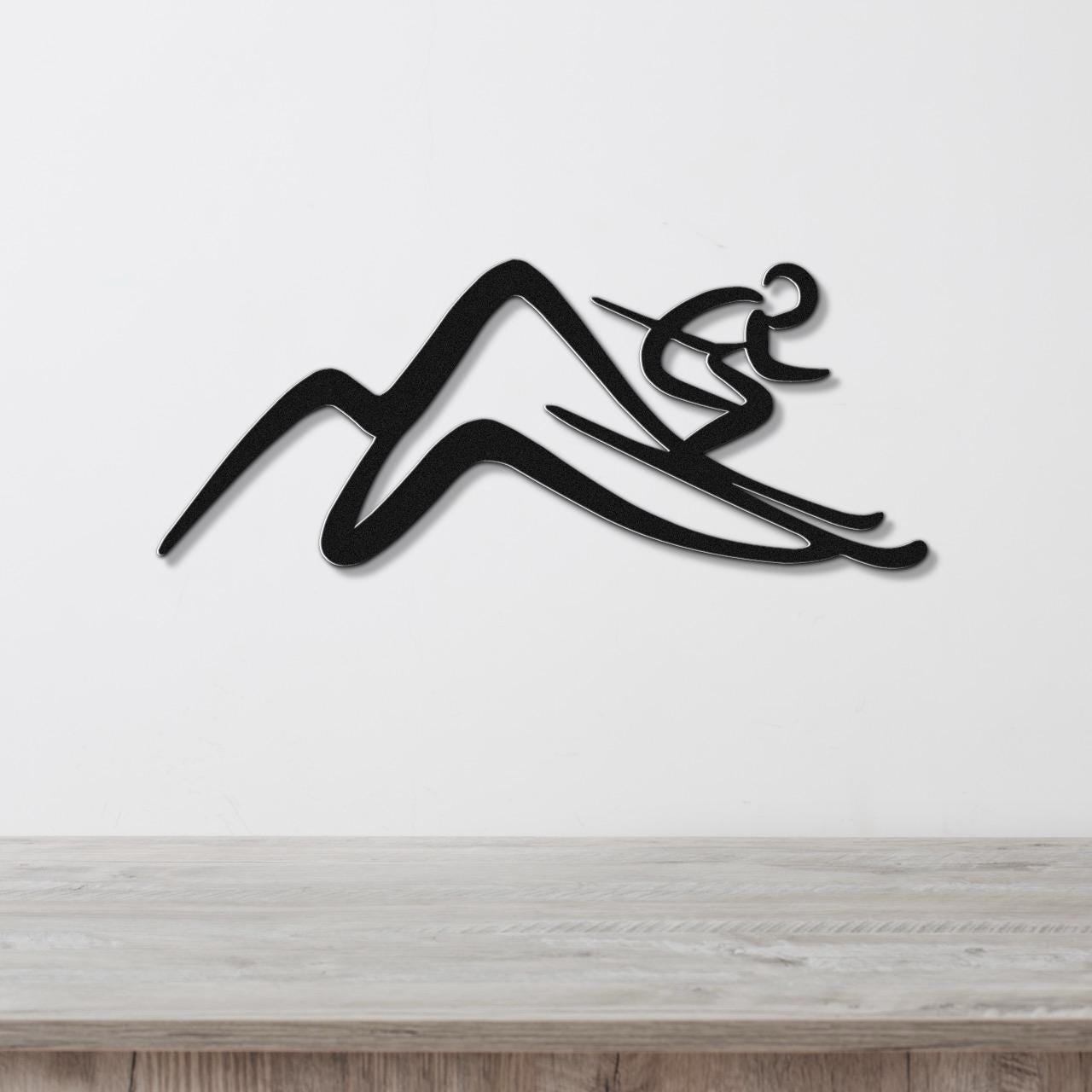 Black metal wall art featuring a skier silhouette gliding over mountain peaks, mounted on a white wall above a light wood counter.
