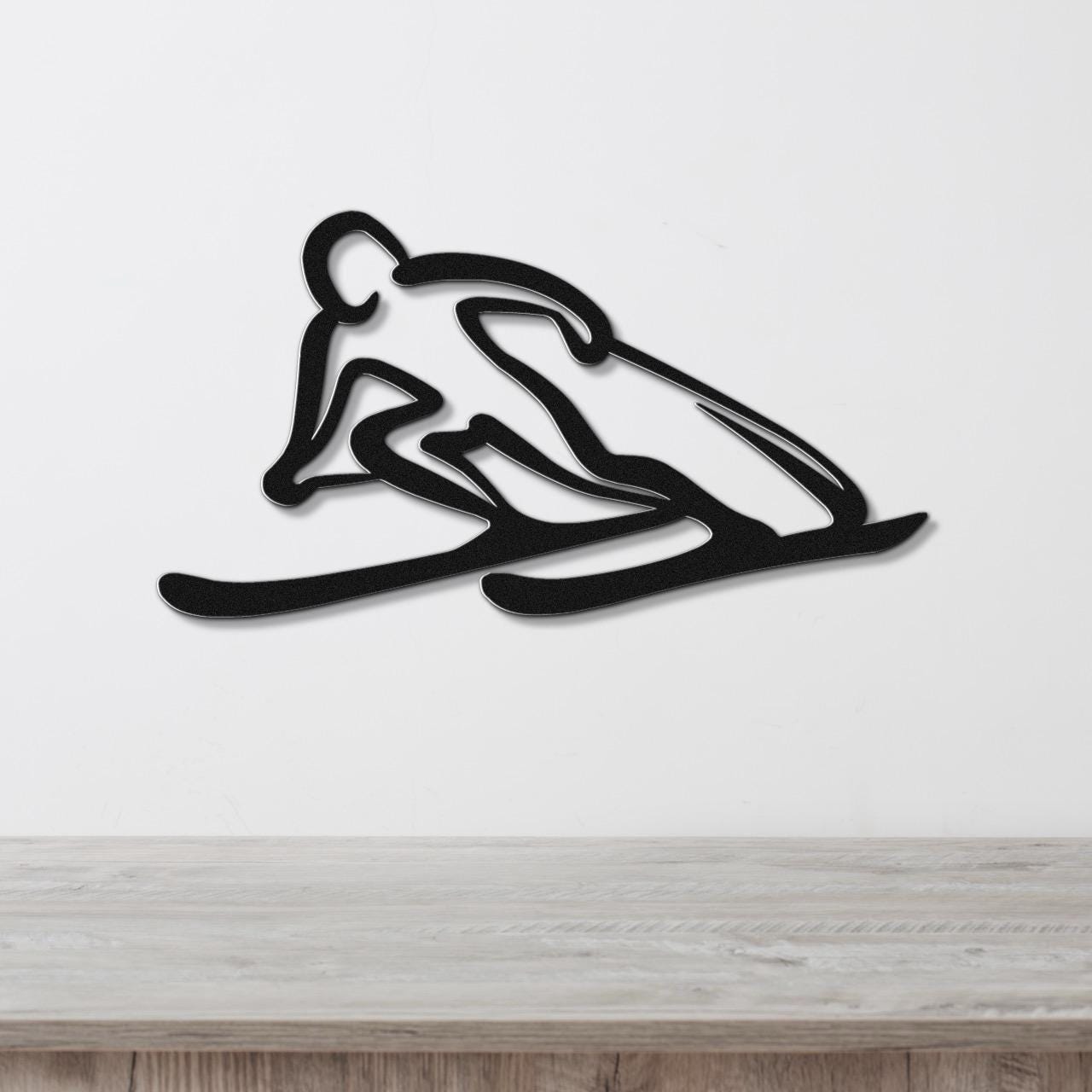 Black metal wall art of a skier silhouette with motion-line cutouts, mounted on a white wall above a light wood counter.