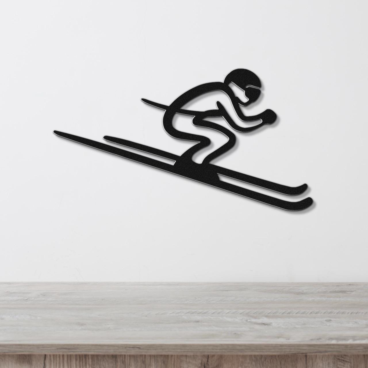 Black metal wall art of a skier silhouette with motion lines, mounted on a white wall above a wooden surface.