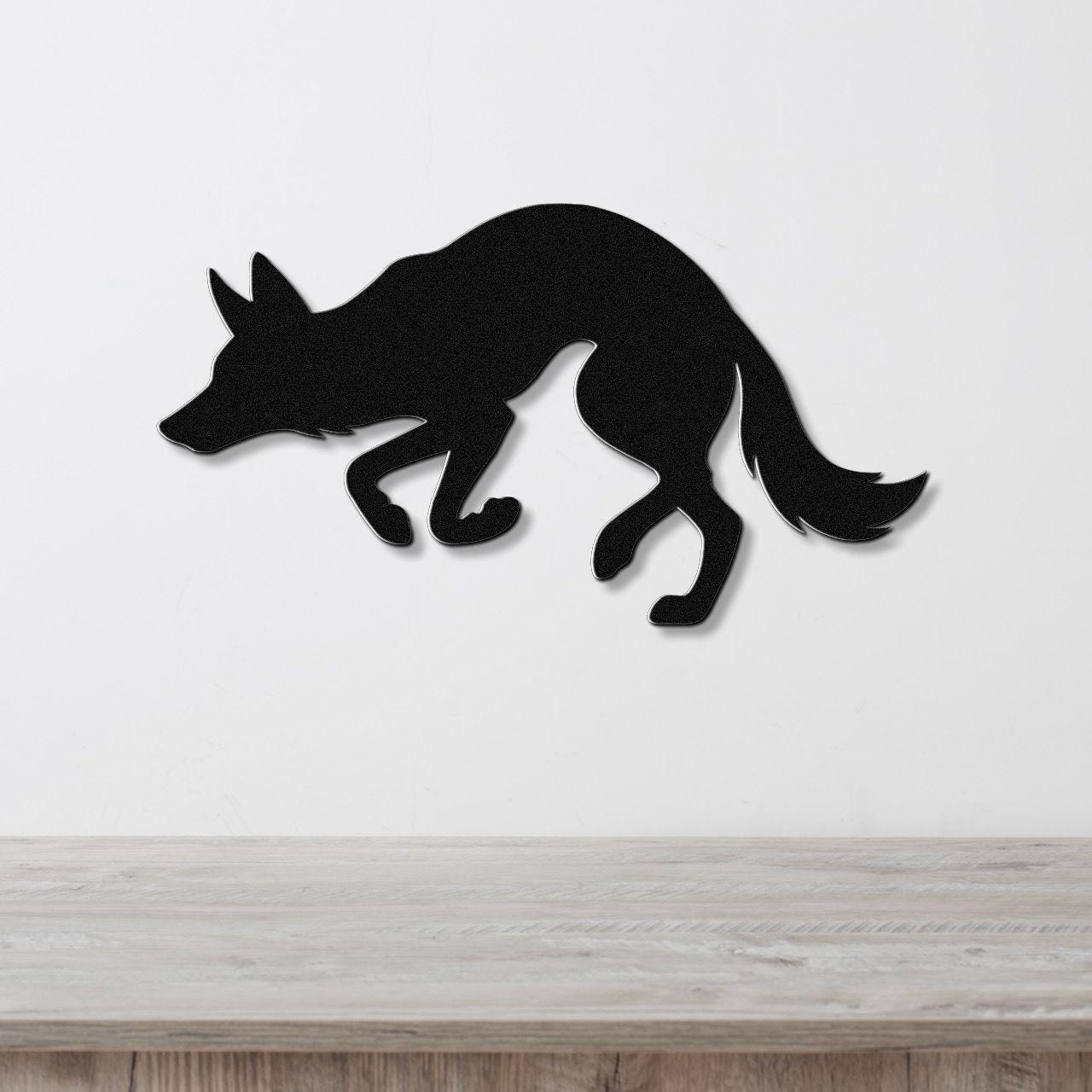 Black metal coyote wall art in a crouching silhouette, mounted on a white wall above a light wood surface.