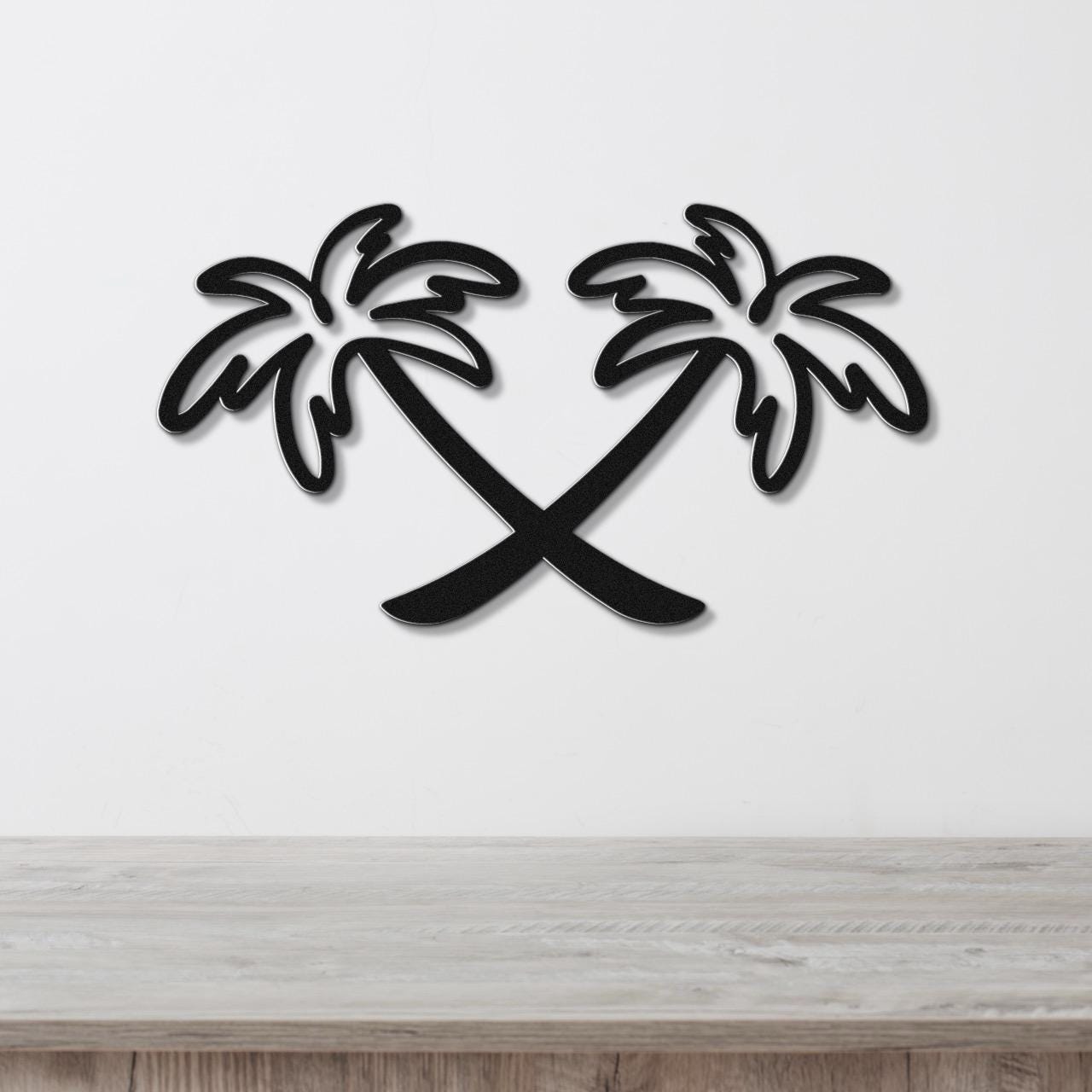 Black metal wall art featuring two crossed palm trees in a silhouette style, mounted on a white wall above a light wood surface.