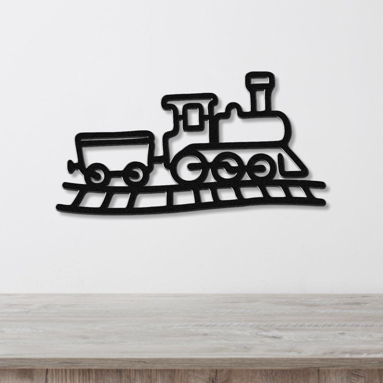 Black metal train wall art with a silhouette design of a locomotive and car on tracks, mounted on a white wall above a wooden surface.