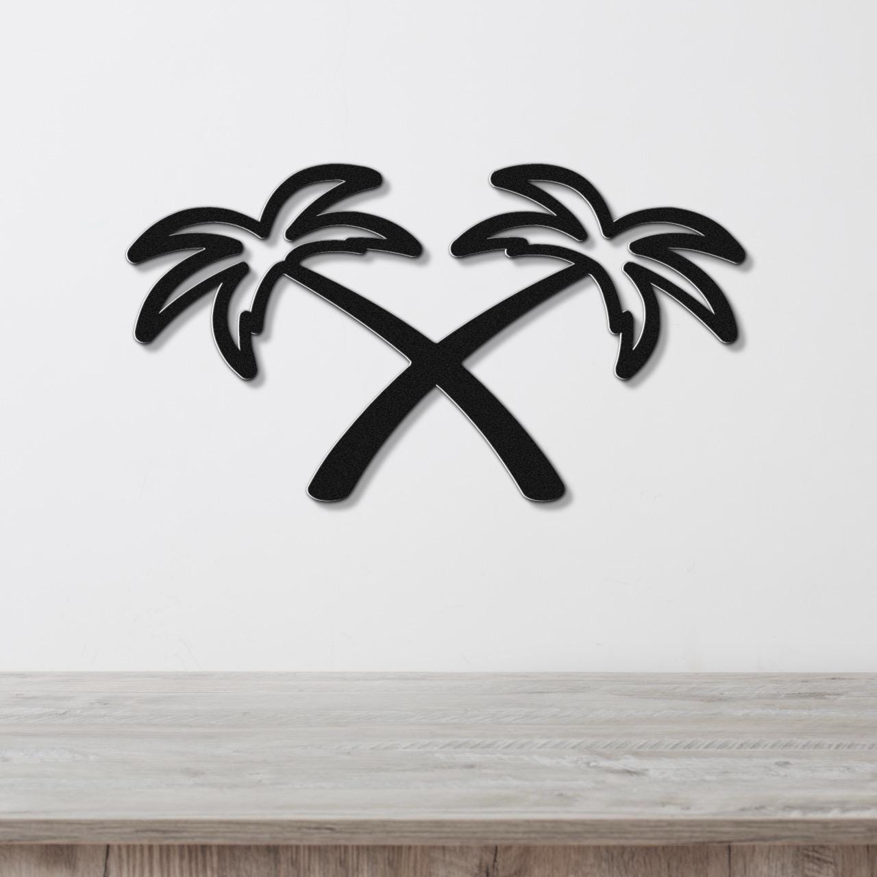 Black metal wall art featuring two crossed palm trees in a silhouette style, mounted on a white wall above a light wood surface.
