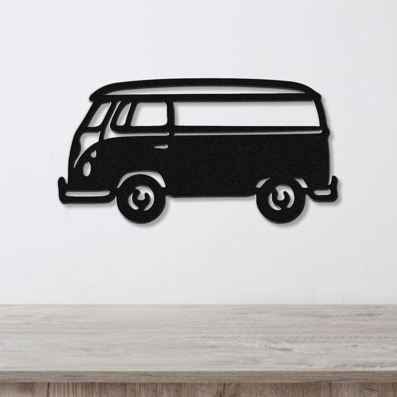 Black metal wall art cutout of a vintage van with visible windows and wheels, mounted on a white wall above a light wood surface.