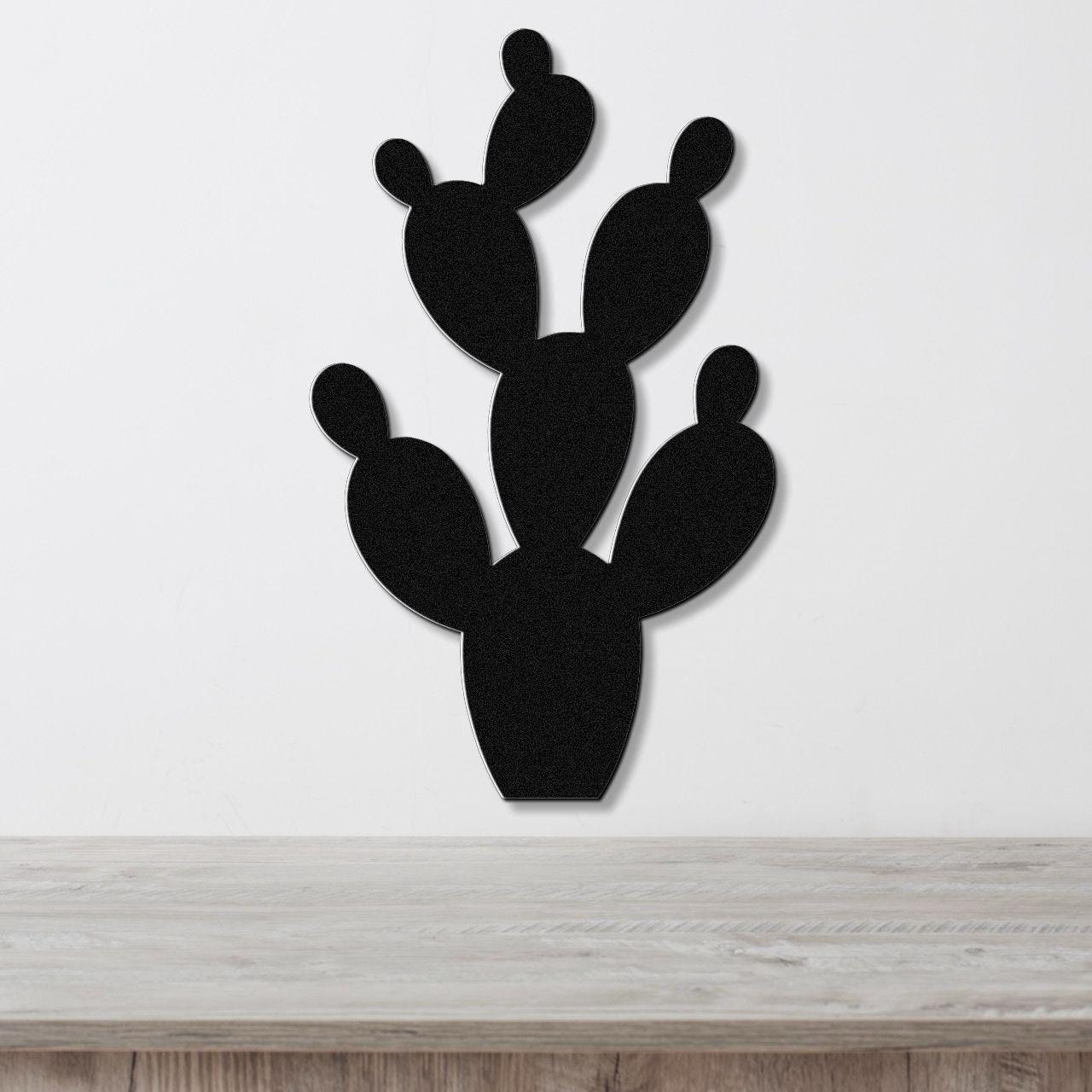 Black metal prickly pear cactus wall art with cutout pads, mounted on a white wall above a light wood counter.