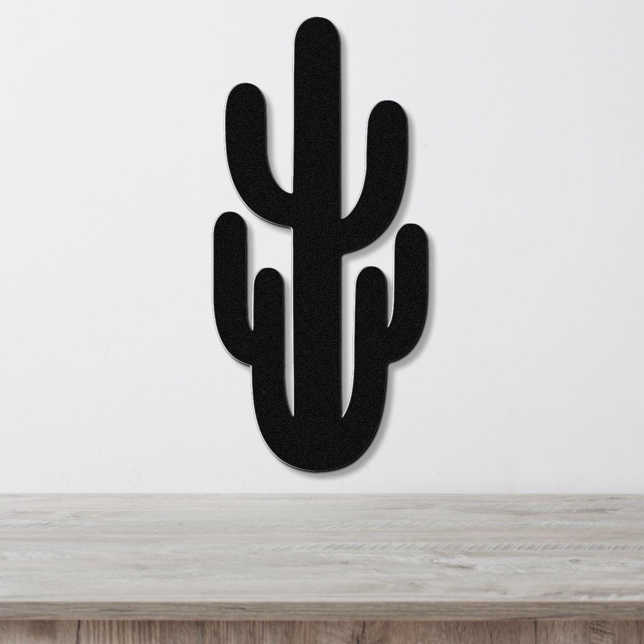Black metal Saguaro cactus wall art with cutout arms, mounted on a white wall above a light wood counter.