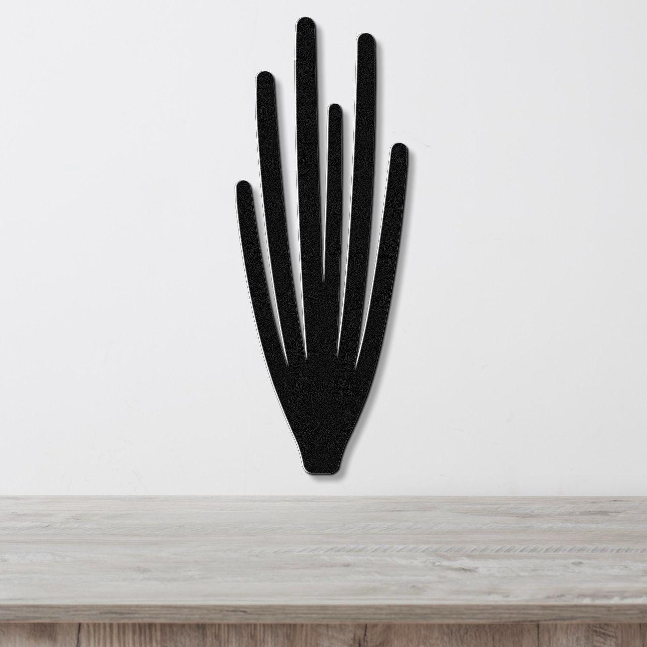 Black metal wall art cutout of an organ pipe cactus with vertical spines, mounted on a white wall above a light wood surface.