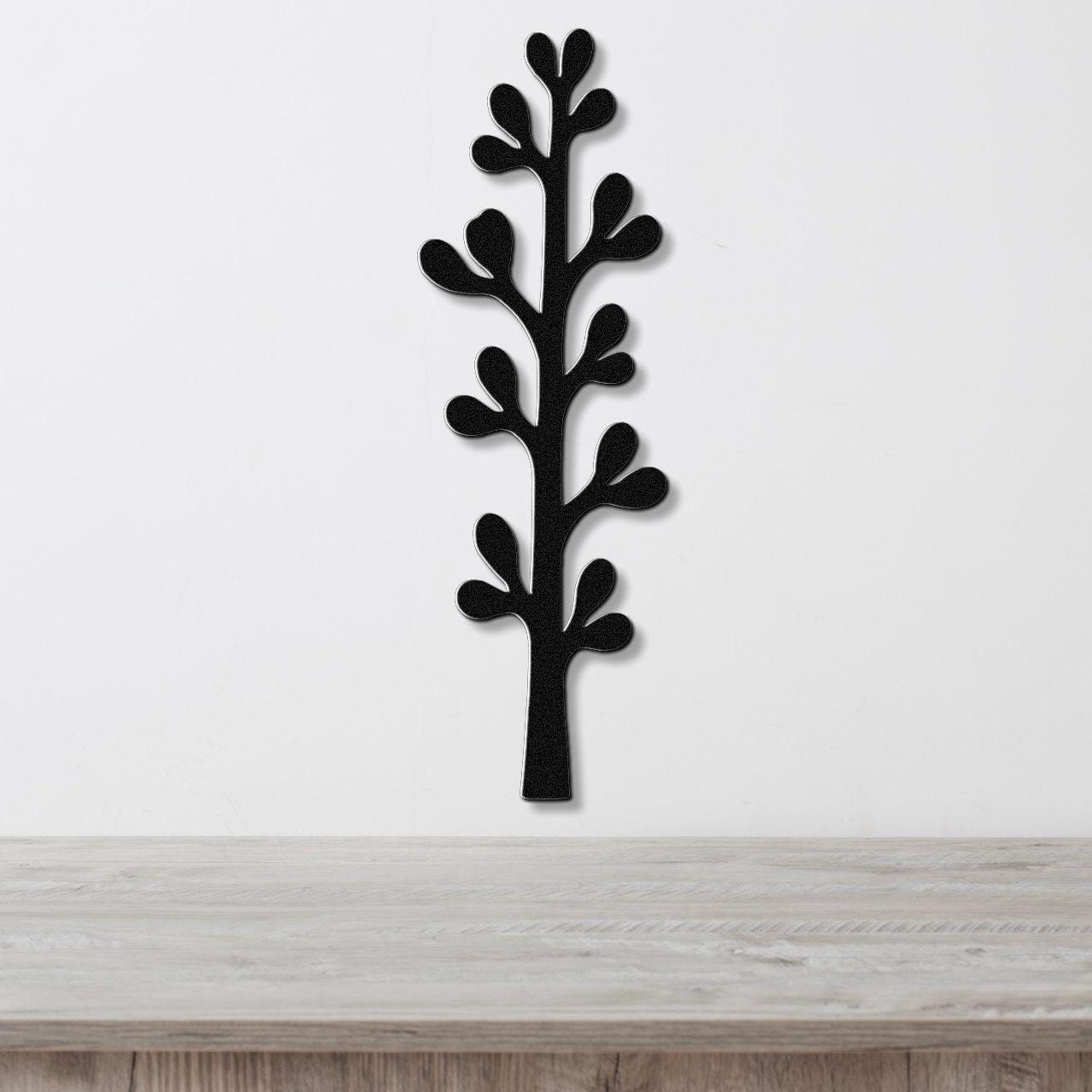 Black metal wall art in a silhouette of an olive branch with leaf cutouts, mounted on a white wall above a light wood surface.