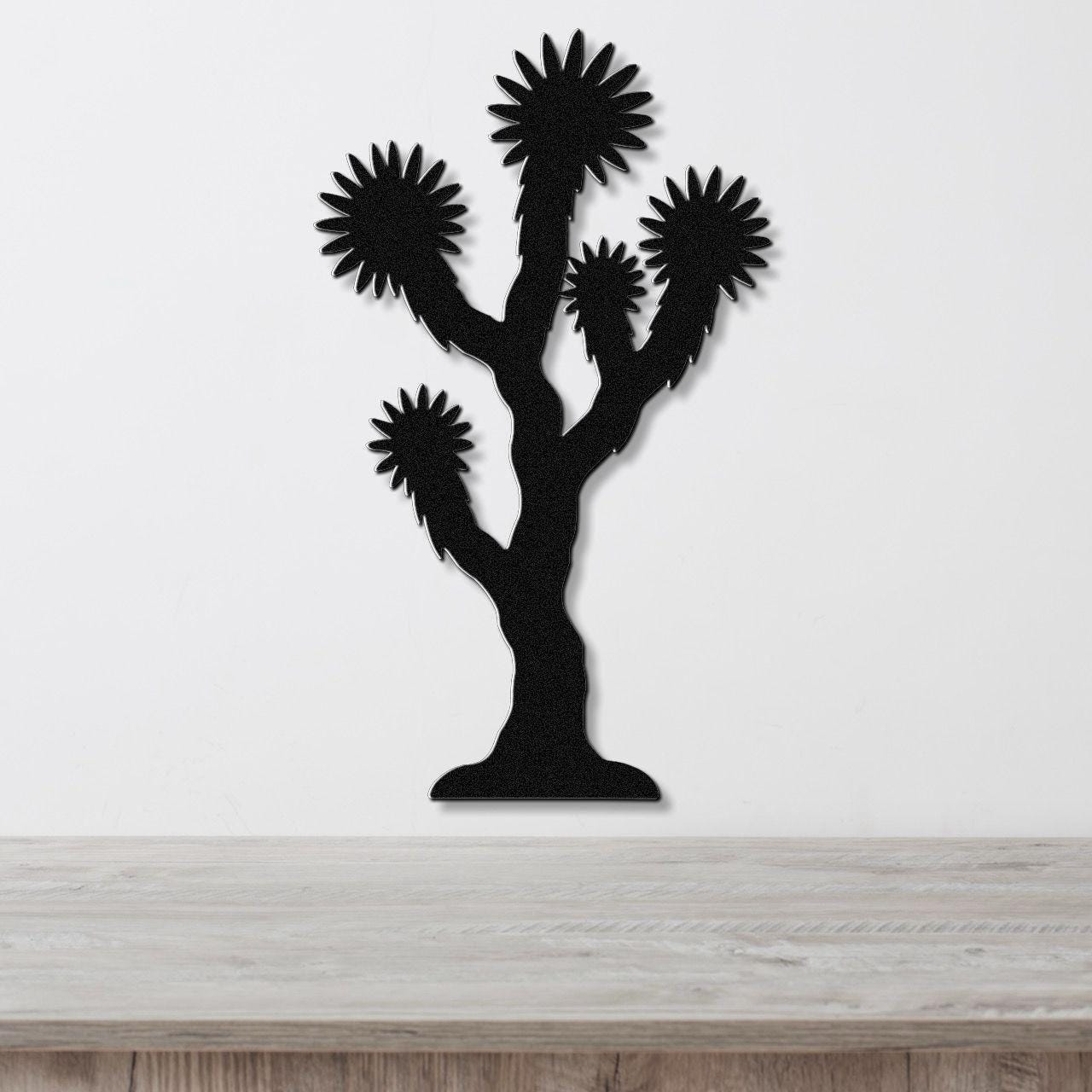 Black metal Joshua tree wall art with spiky branch cutouts, mounted on a white wall above a light wood countertop.