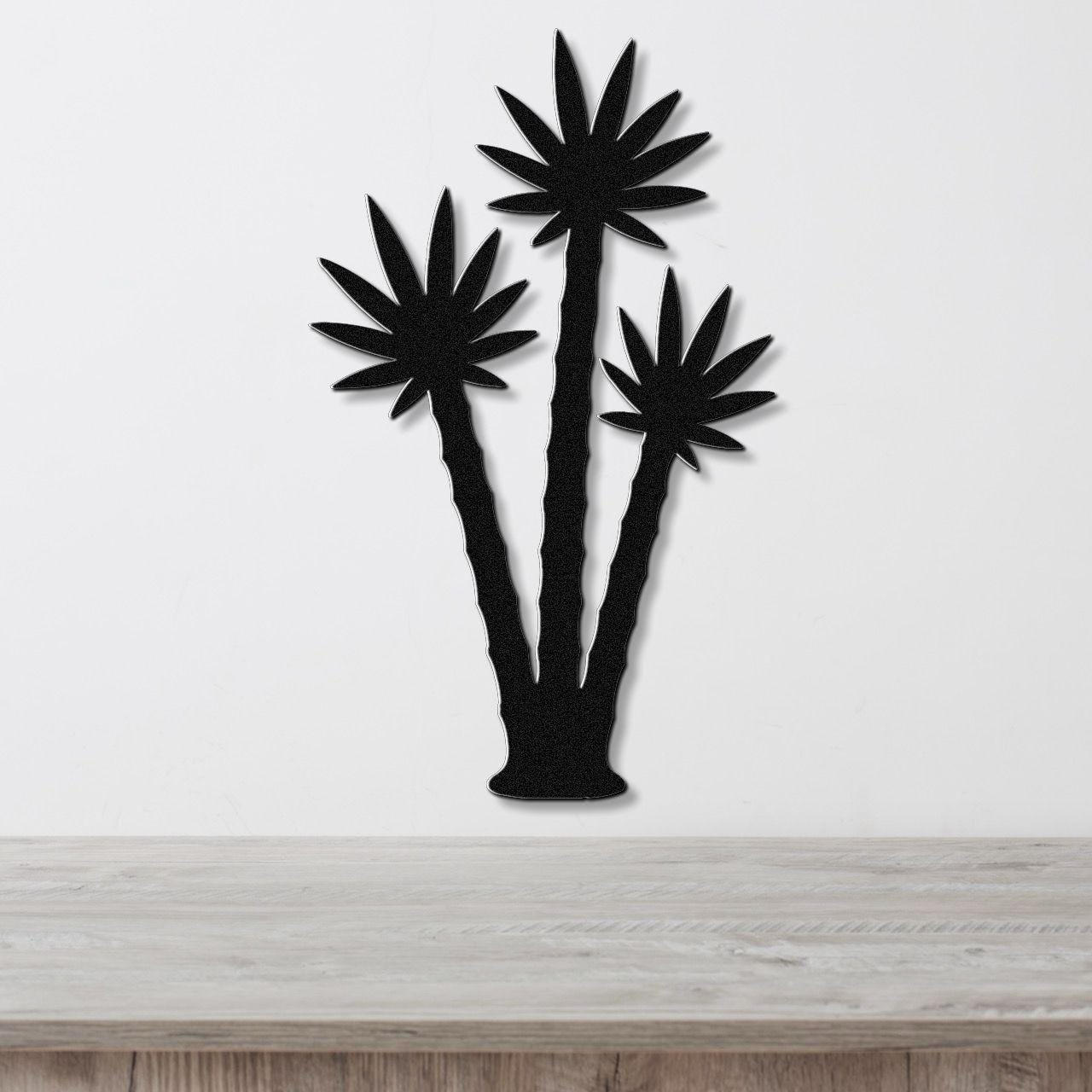 Black metal wall art featuring a silhouette of three palm trees with leaf cutouts, mounted on a white wall above a wooden surface.