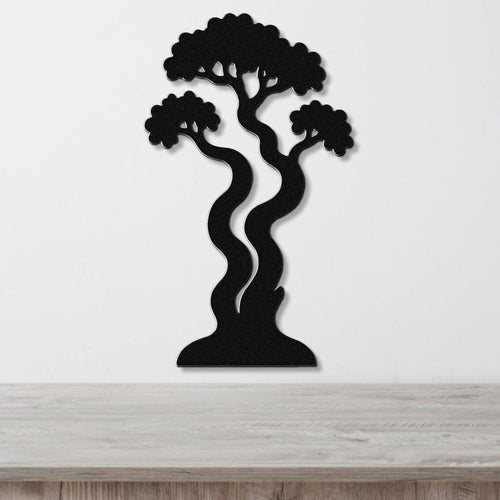Black metal wall art in a bonsai tree silhouette with wavy trunk and layered branches, mounted on a white wall above a light wood surface.