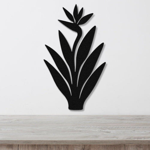 Black metal Bird of Paradise wall art with a silhouette cutout of leaves and flower, mounted on a white wall above a light wood counter.