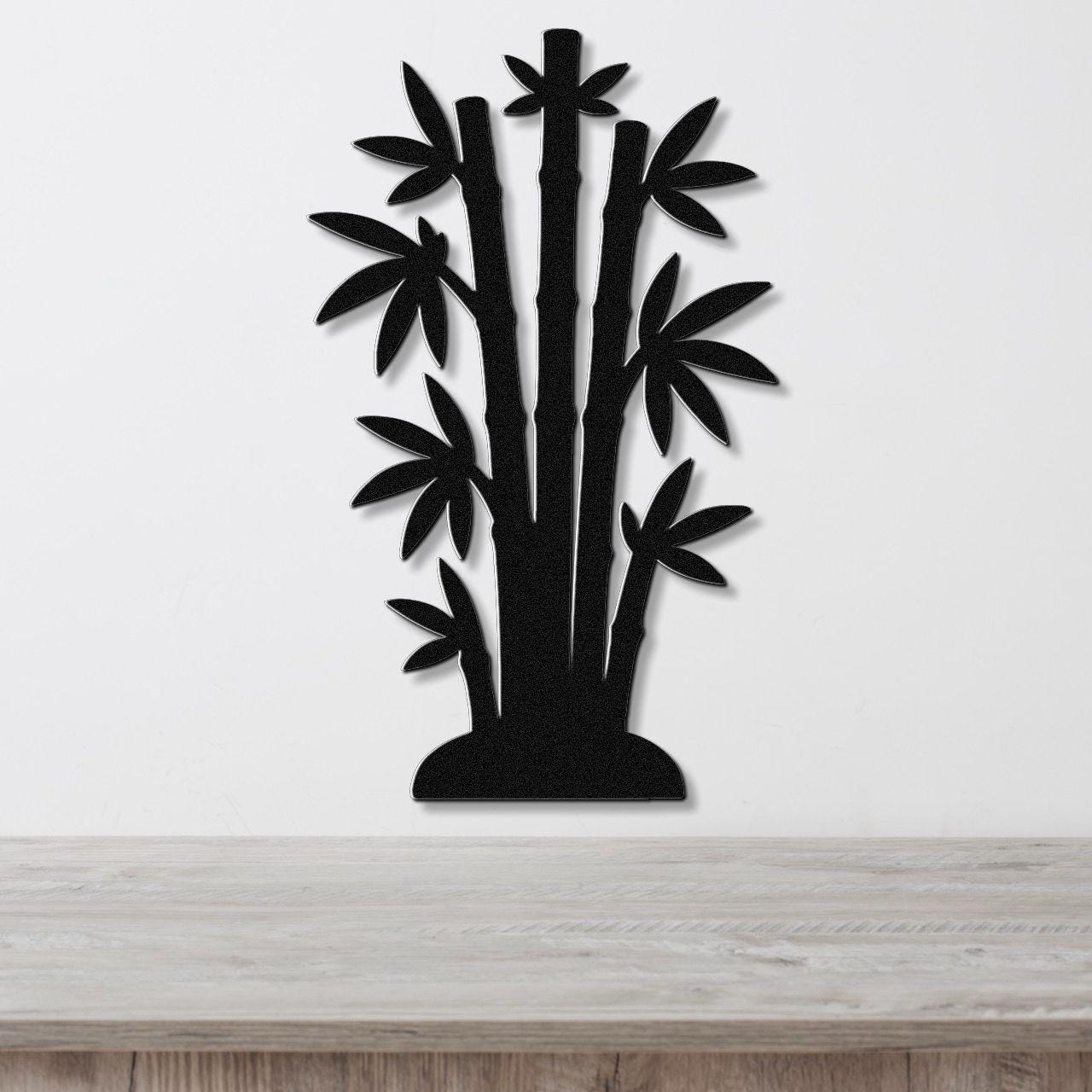Black metal wall art cutout of a bamboo cluster with multiple stalks and leaves, mounted on a white wall above a light wood surface.