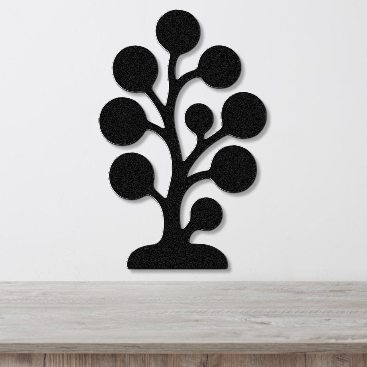 Black metal wall art in a tree silhouette with circular cutouts, mounted on a white wall above a light wood counter.