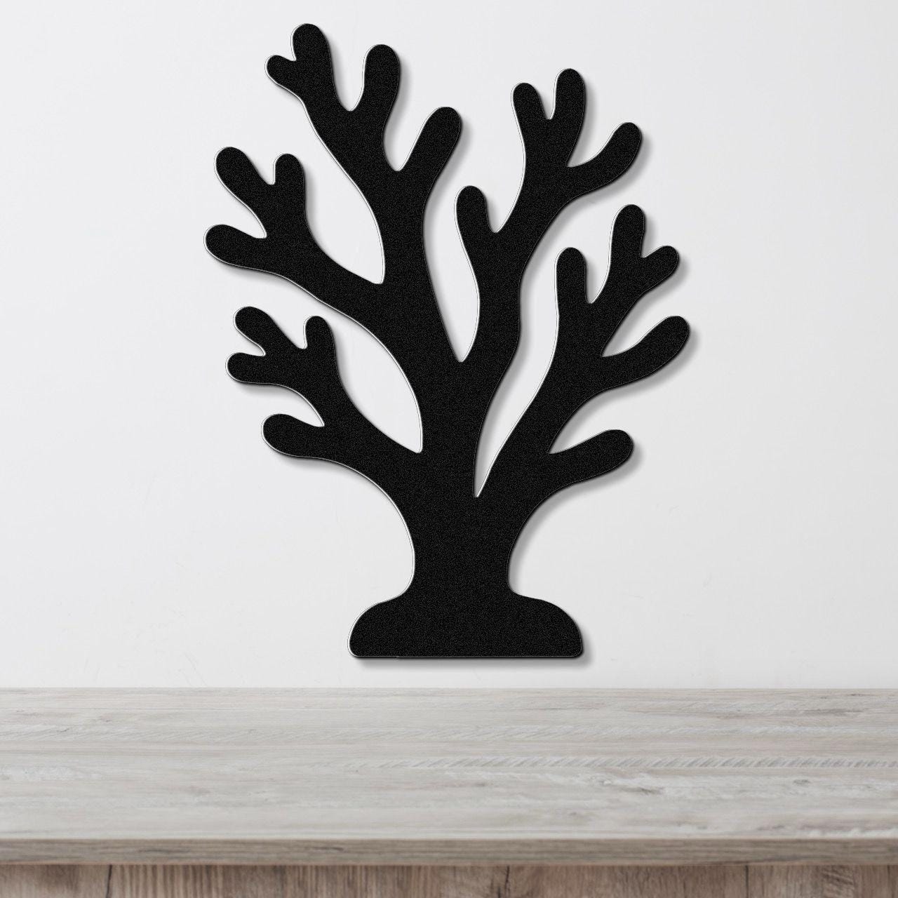 Black metal coral wall art with branching cutouts, mounted on a white wall above a light wood surface.