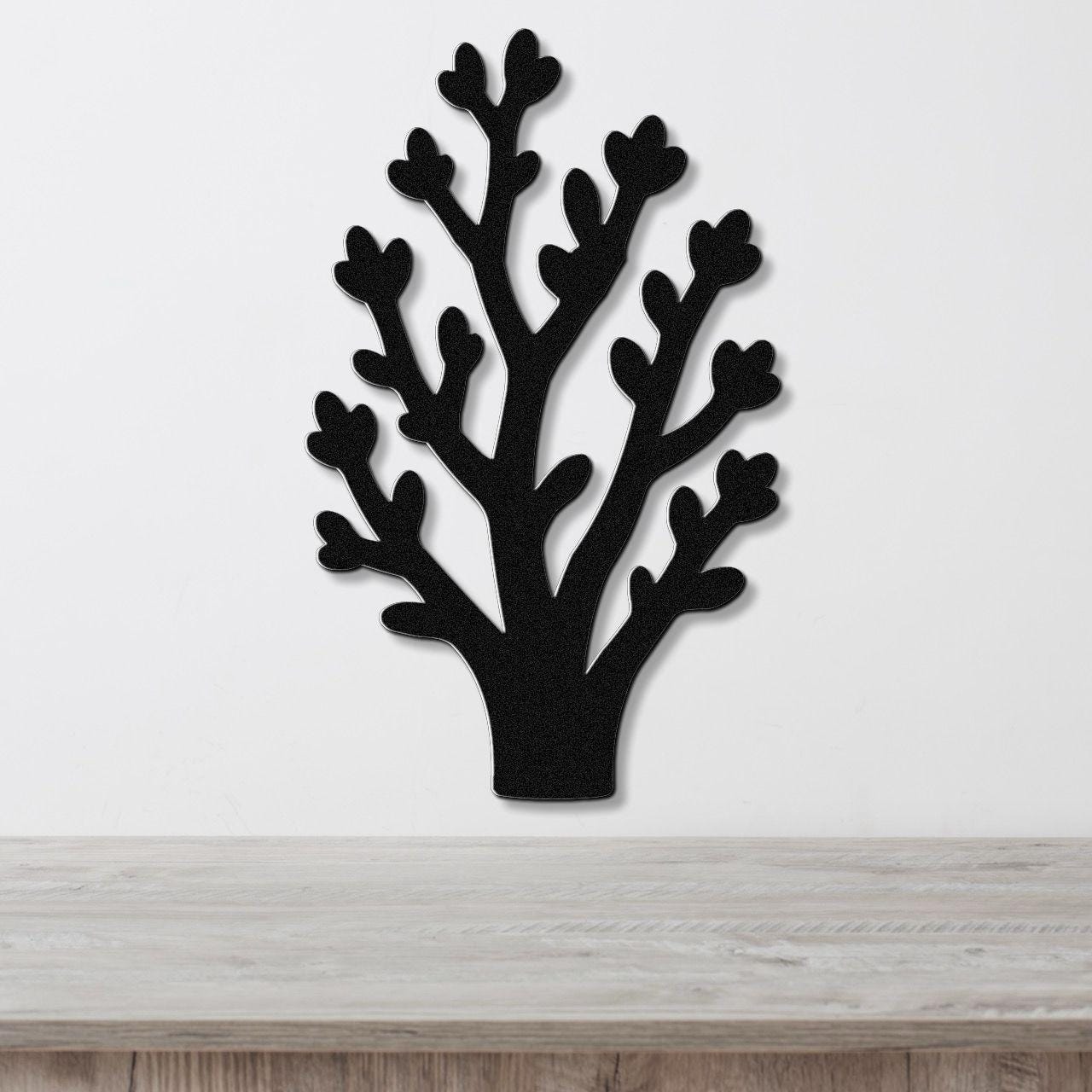 Black metal wall art in a tree silhouette with branching cutouts, mounted on a white wall above a light wood surface.