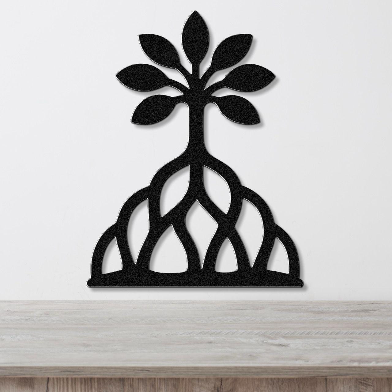 Black metal wall art in the shape of a tree with leafy top and exposed root system, mounted on a white wall above a wooden surface.