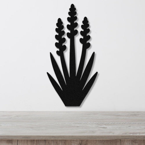 Black metal wall art in a yucca plant silhouette with three tall flower spikes and spiky leaves, mounted on a white wall above a light wood surface.