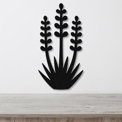 Black metal wall art cutout of a yucca plant with three tall stems and spiky base, mounted on a white wall above a light wood surface.