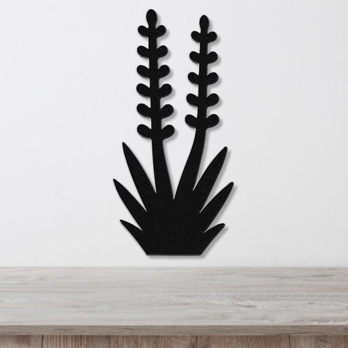 Black metal wall art in the silhouette of a yucca plant with two tall flower stalks and spiky leaves, mounted on a white wall above a wooden surface.