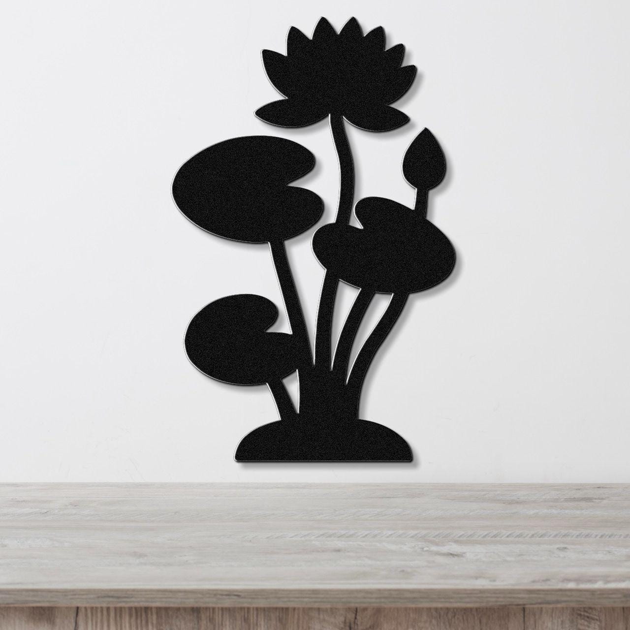Black metal wall art silhouette of a lotus water lily with multiple leaves and a blooming flower, mounted on a white wall above a light wood surface.