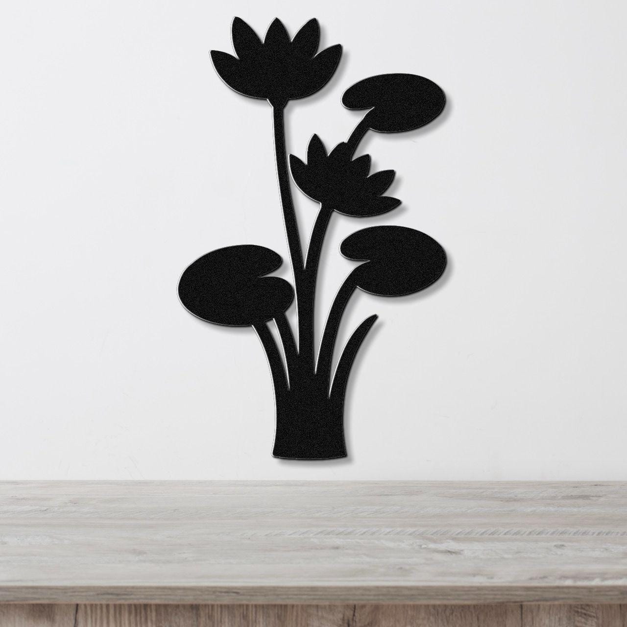 Black metal wall art featuring a lotus water lily silhouette with cutout flowers and leaves, mounted on a white wall above a wooden surface.