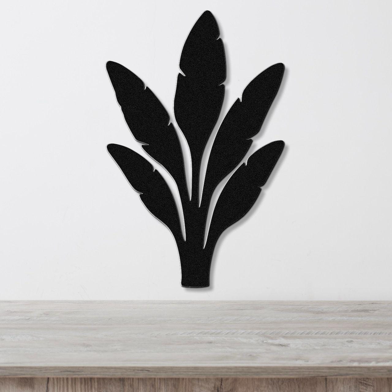 Black metal wall art in a banana plant silhouette with layered leaf cutouts, mounted on a white wall above a light wood surface.