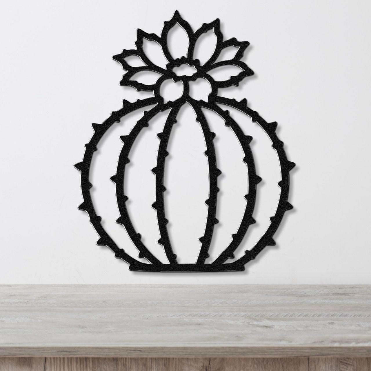 Black metal barrel cactus wall art with flower and spine cutouts, mounted on a white wall above a light wood counter.