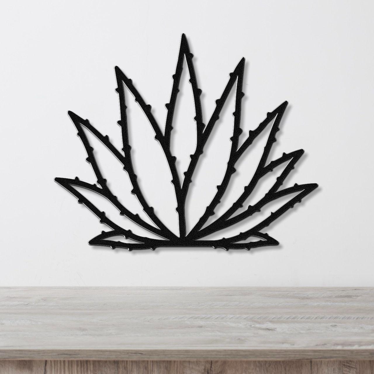Black metal agave wall art with spiky leaf cutouts, mounted on a white wall above a light wood surface.