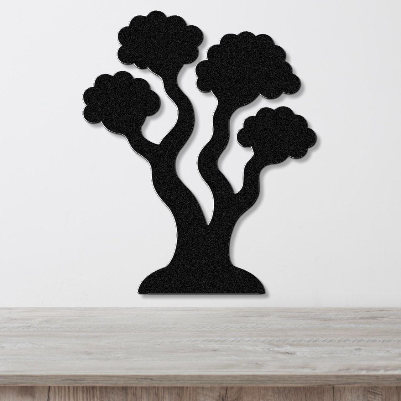 Black metal wall art in a stylized tree silhouette with three rounded canopies and curved trunks, mounted on a white wall above a light wood surface.