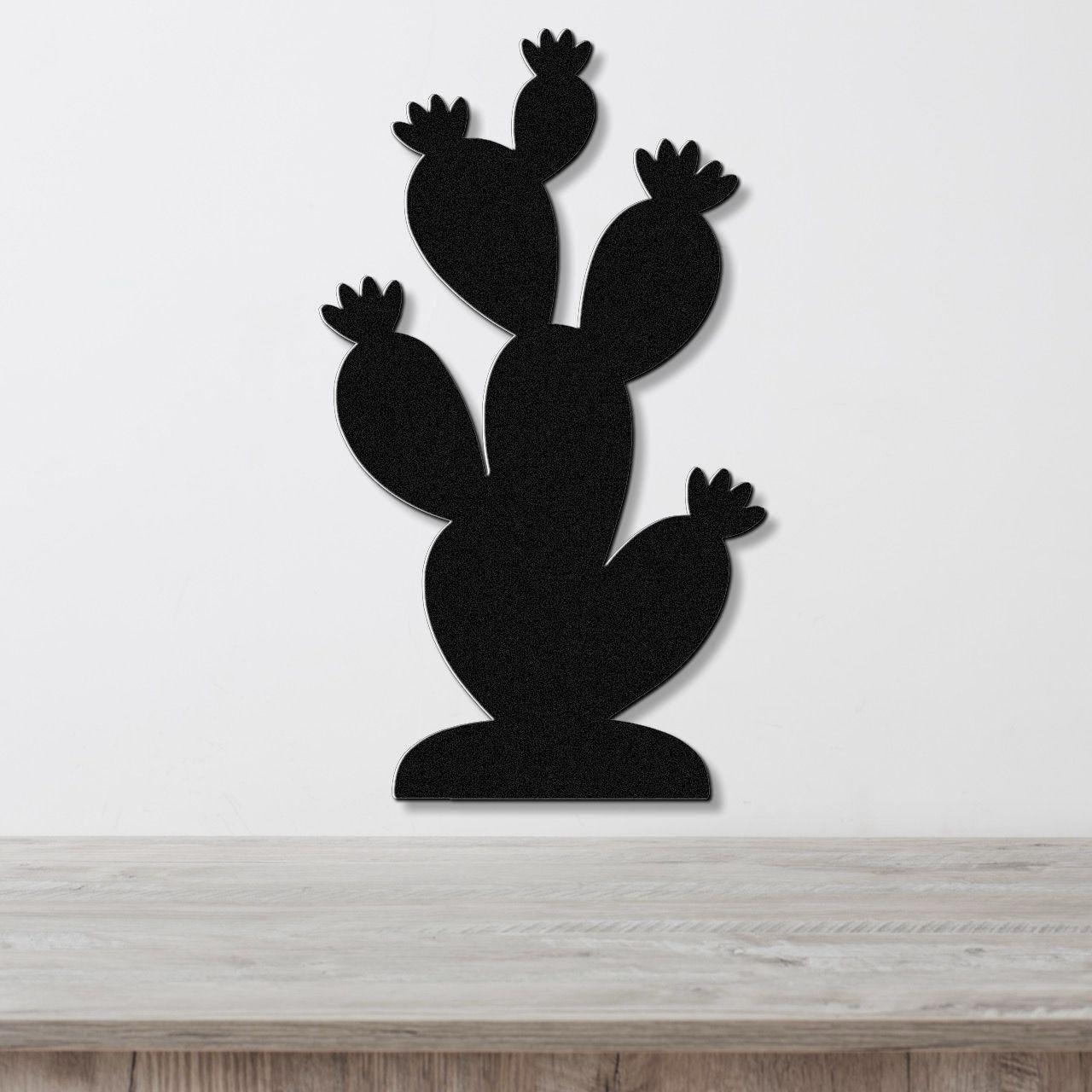 Black metal cactus wall art with multiple paddle-shaped arms and flower cutouts, mounted on a white wall above a light wood surface.