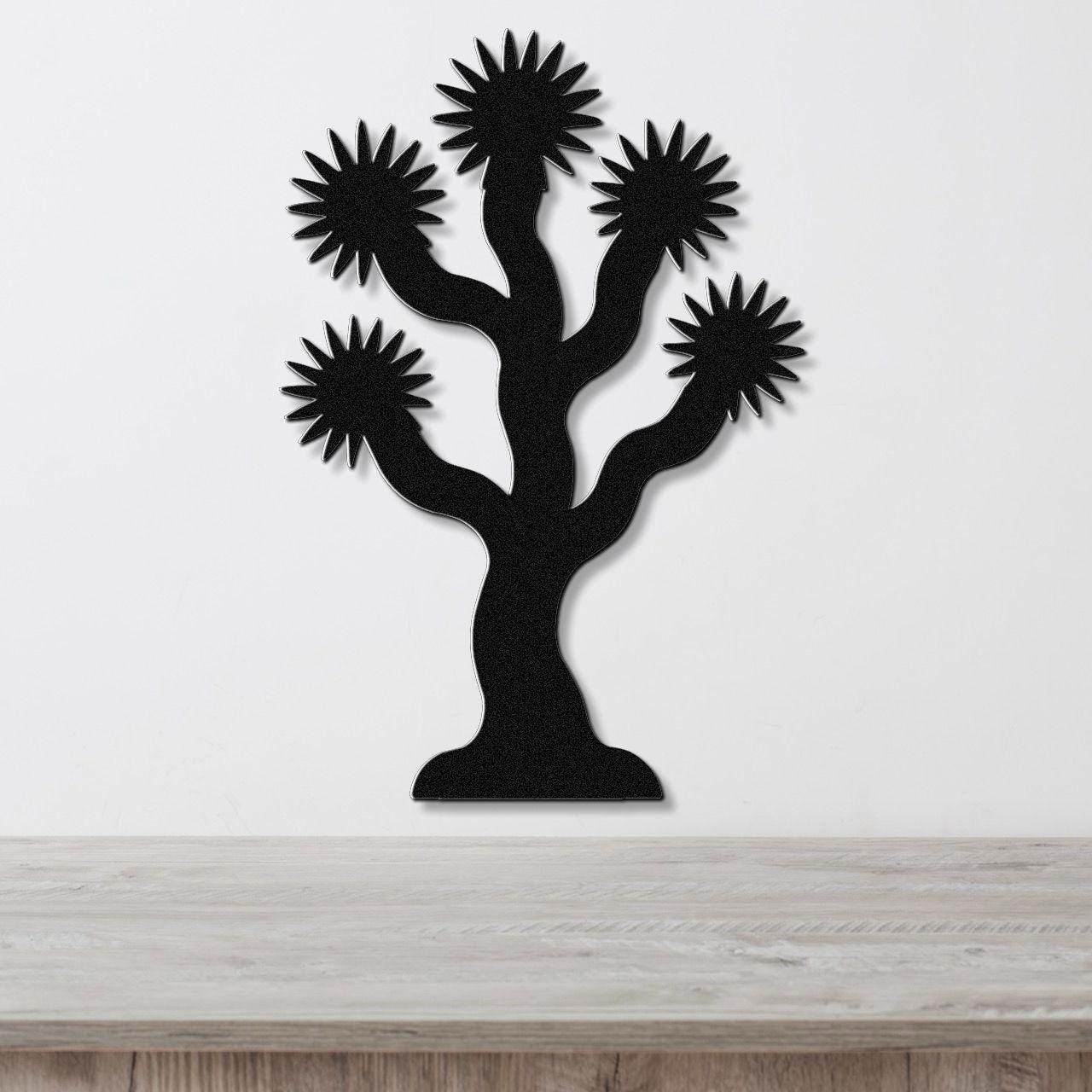 Black metal wall art in the silhouette of a Joshua tree with starburst-shaped branches, mounted on a white wall above a light wood surface.