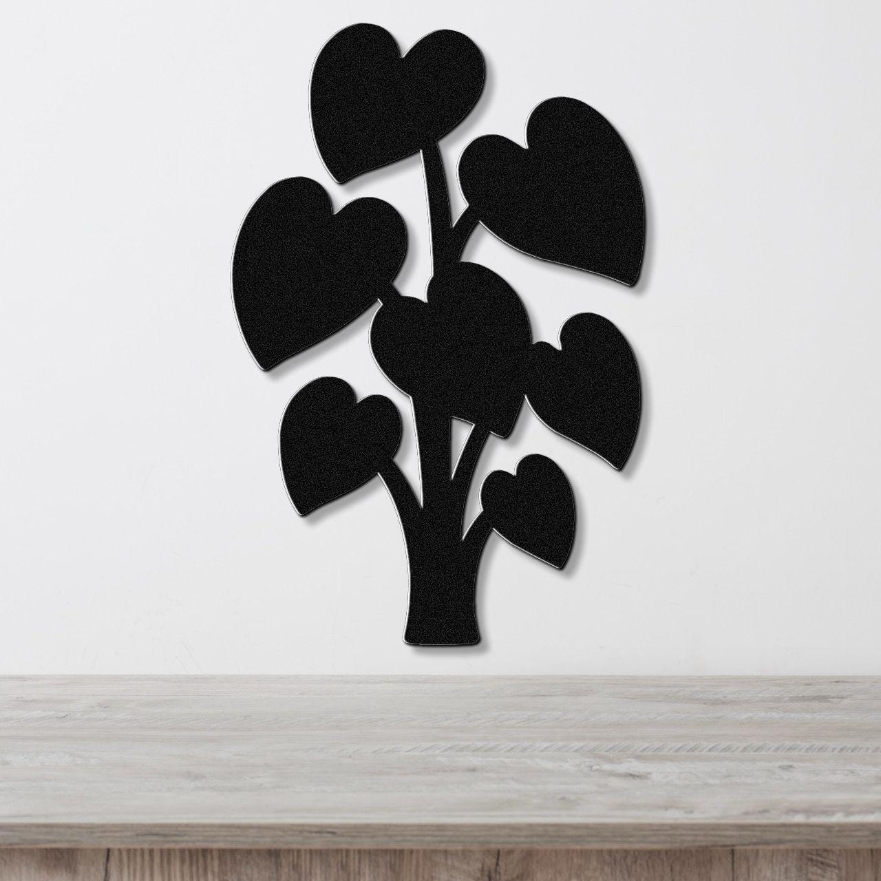 Black metal wall art shaped like a plant with heart-shaped leaves, mounted on a white wall above a wooden surface.