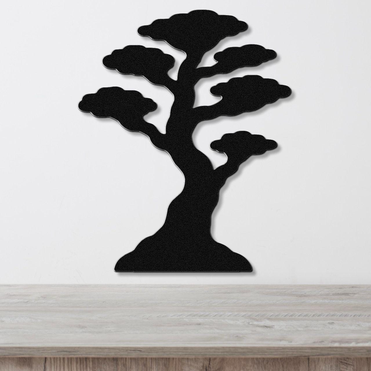 Black metal wall art in the silhouette of a bonsai tree with layered cloud-like branches, mounted on a white wall above a wooden surface.