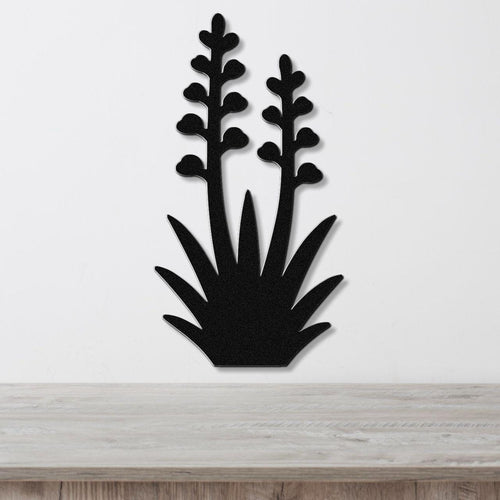 Black metal wall art cutout of a blooming agave plant with two tall flower stalks and spiky base, mounted on a white wall above a light wood surface.