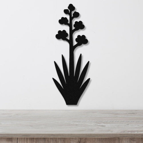 Black metal wall art silhouette of a blooming agave plant with spiky leaves and flower clusters, mounted on a white wall above a light wood surface.