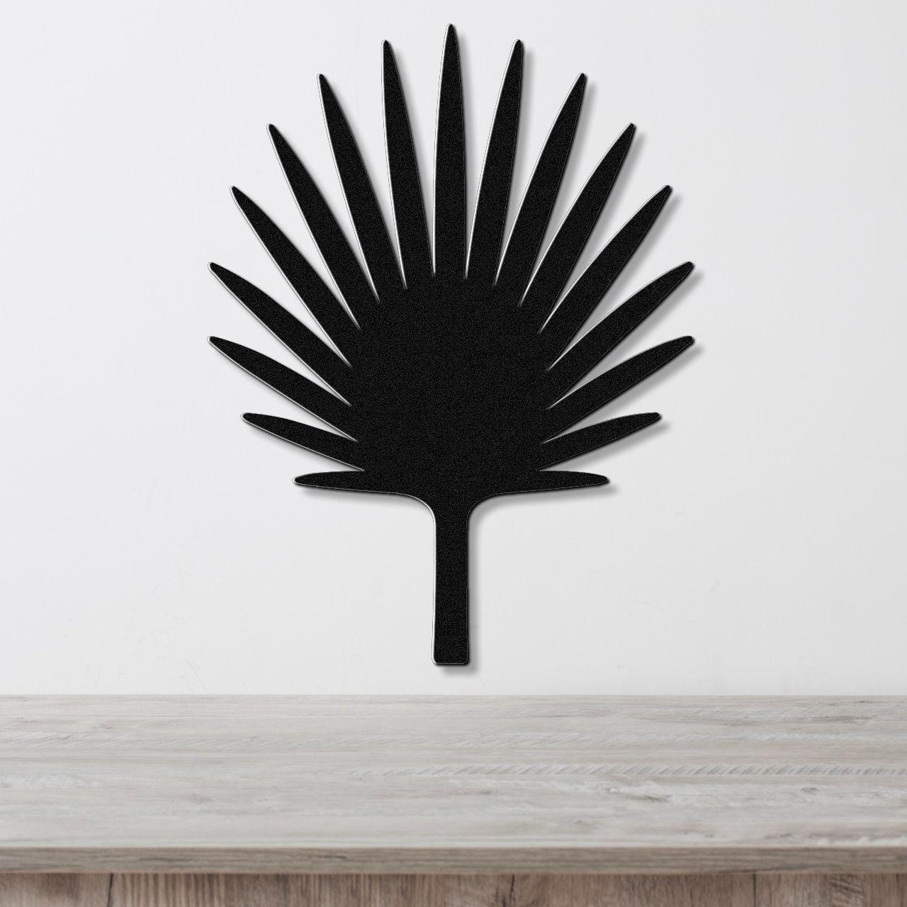 Black metal fan palm tree wall art with radiating leaf cutouts, mounted on a white wall above a light wood surface.
