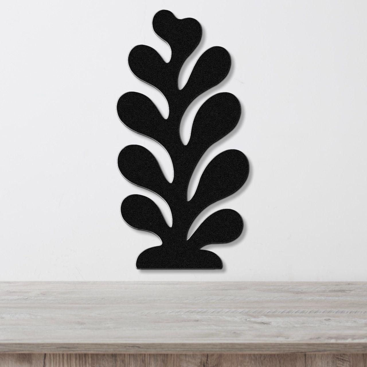 Black metal wall art in a coral or leaf-like silhouette with multiple cutout sections, mounted on a white wall above a light wood surface.