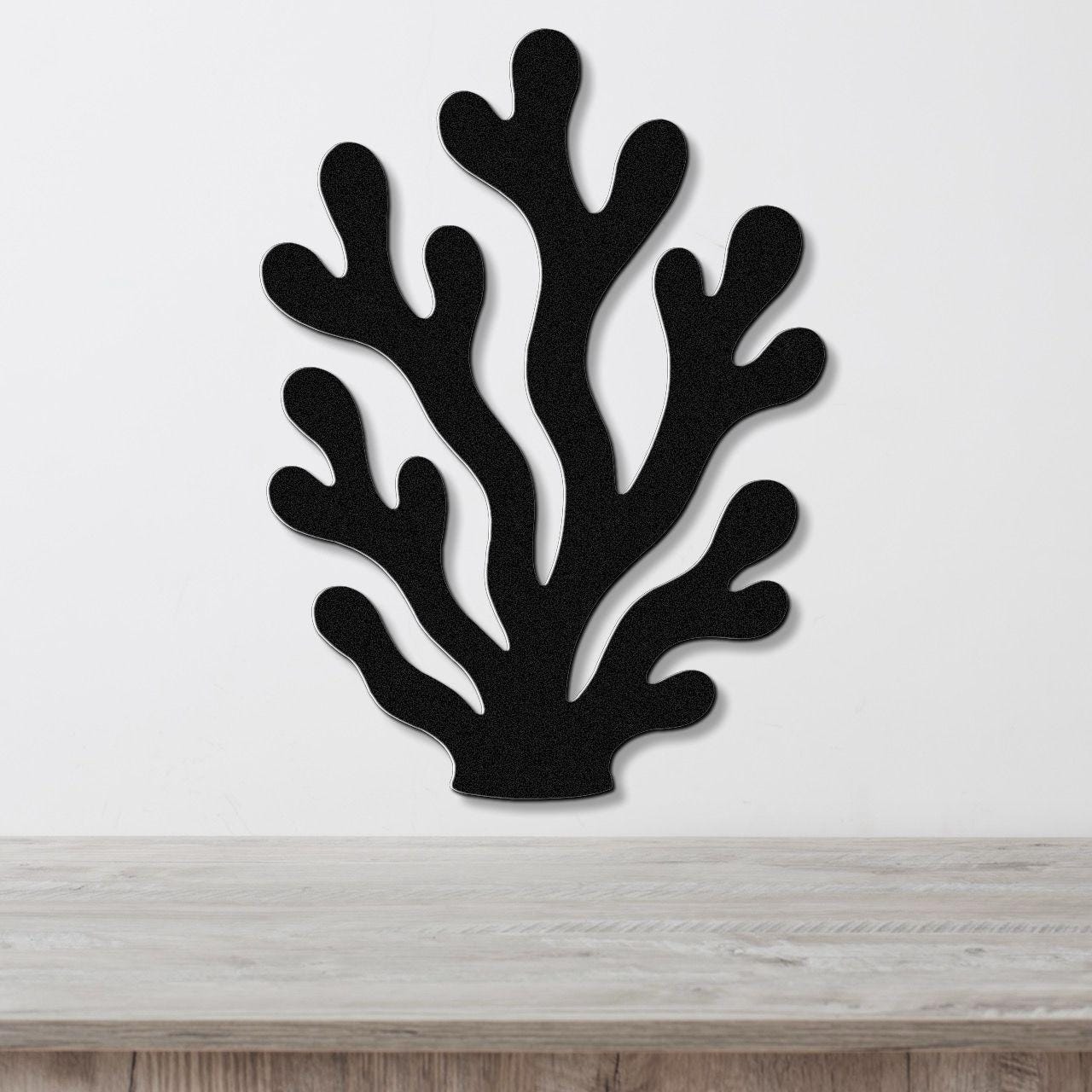 Black metal coral wall art with branching cutouts, mounted on a white wall above a light wood counter.