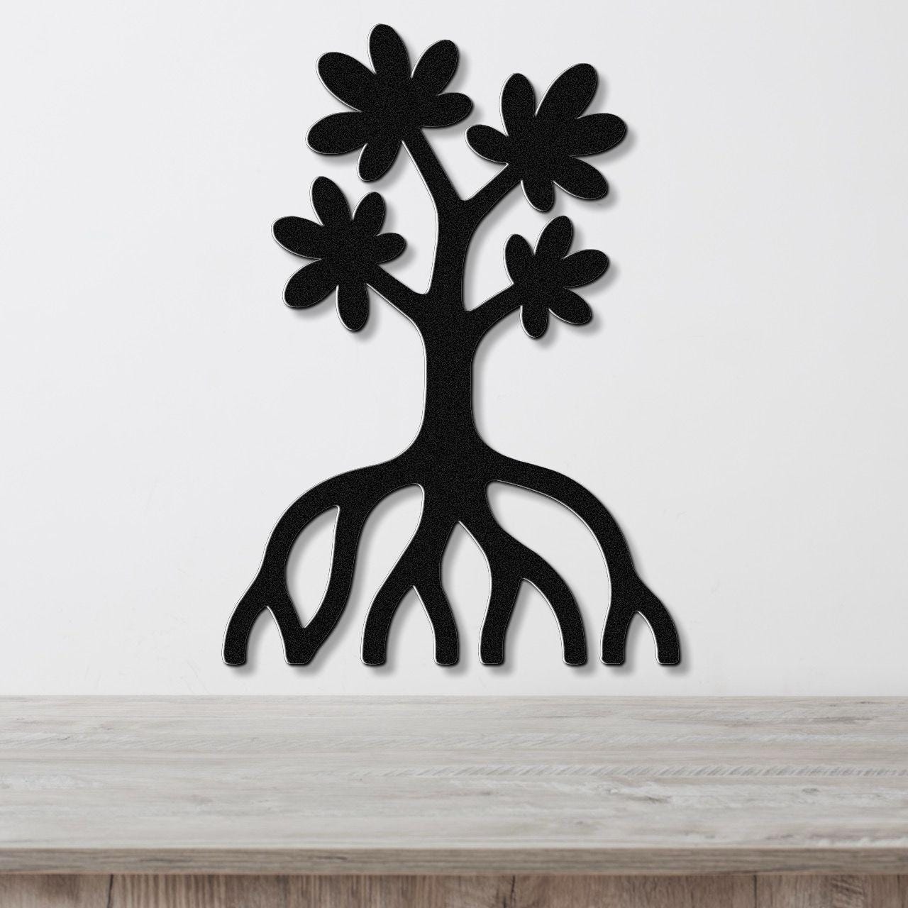 Black metal wall art in the shape of a tree with flower cutouts and exposed roots, mounted on a white wall above a wooden surface.