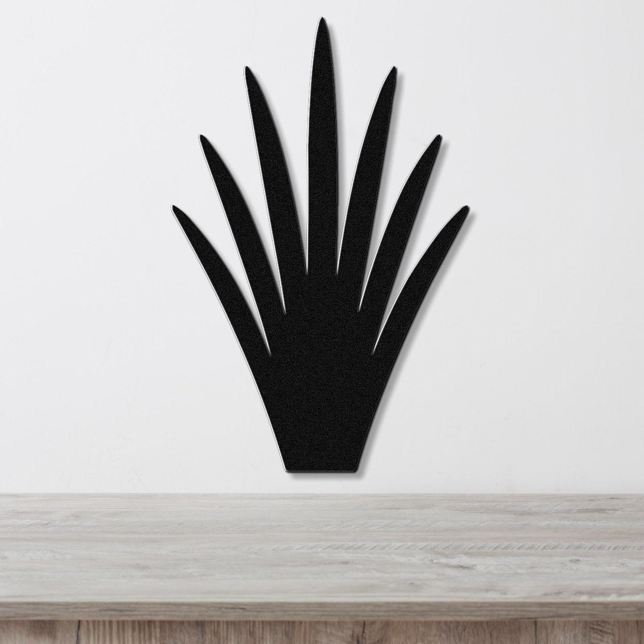 Black metal yucca wall art with pointed leaf cutouts, mounted on a white wall above a light wood surface.