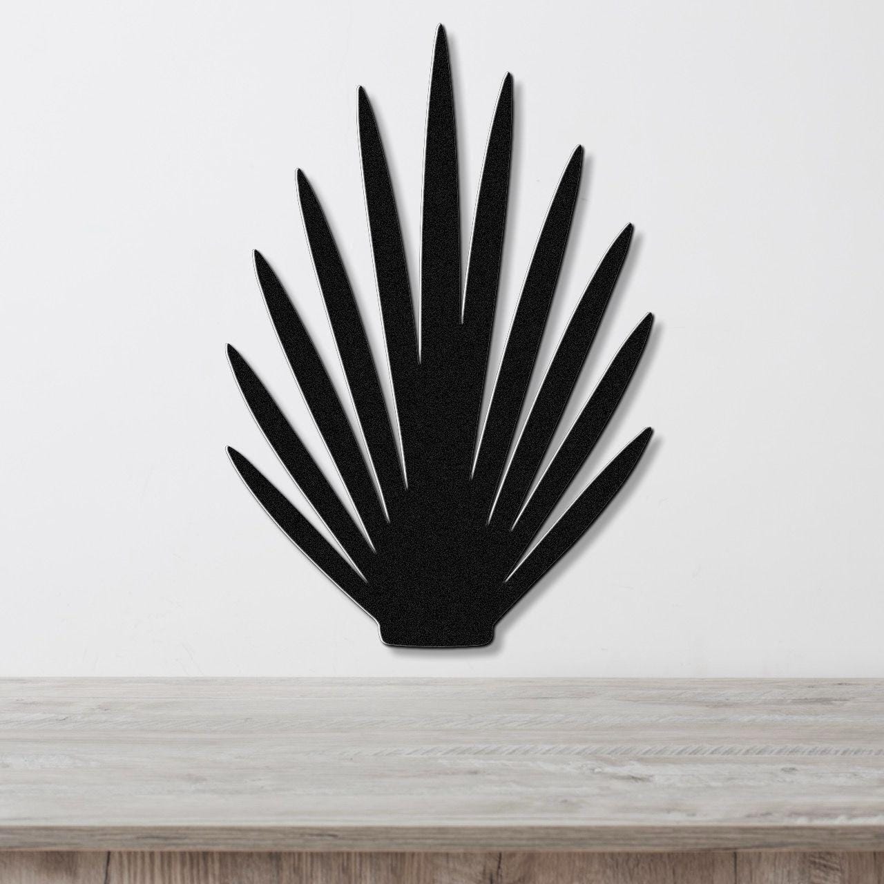 Black metal wall art in a fan-shaped silhouette with pointed rays, mounted on a white wall above a light wood surface.