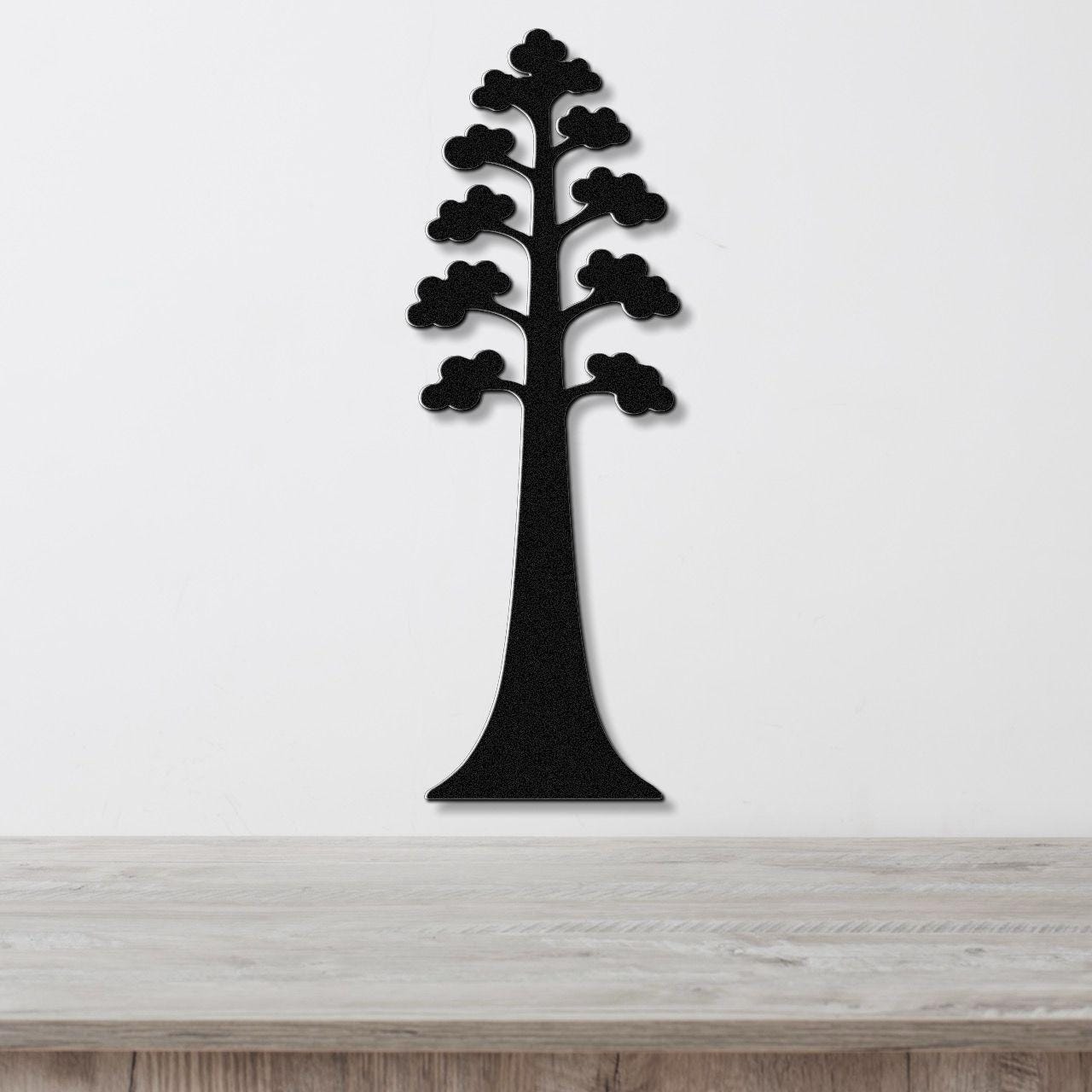 Black metal wall art in the silhouette of a sequoia tree with layered branches, mounted on a white wall above a wooden surface.