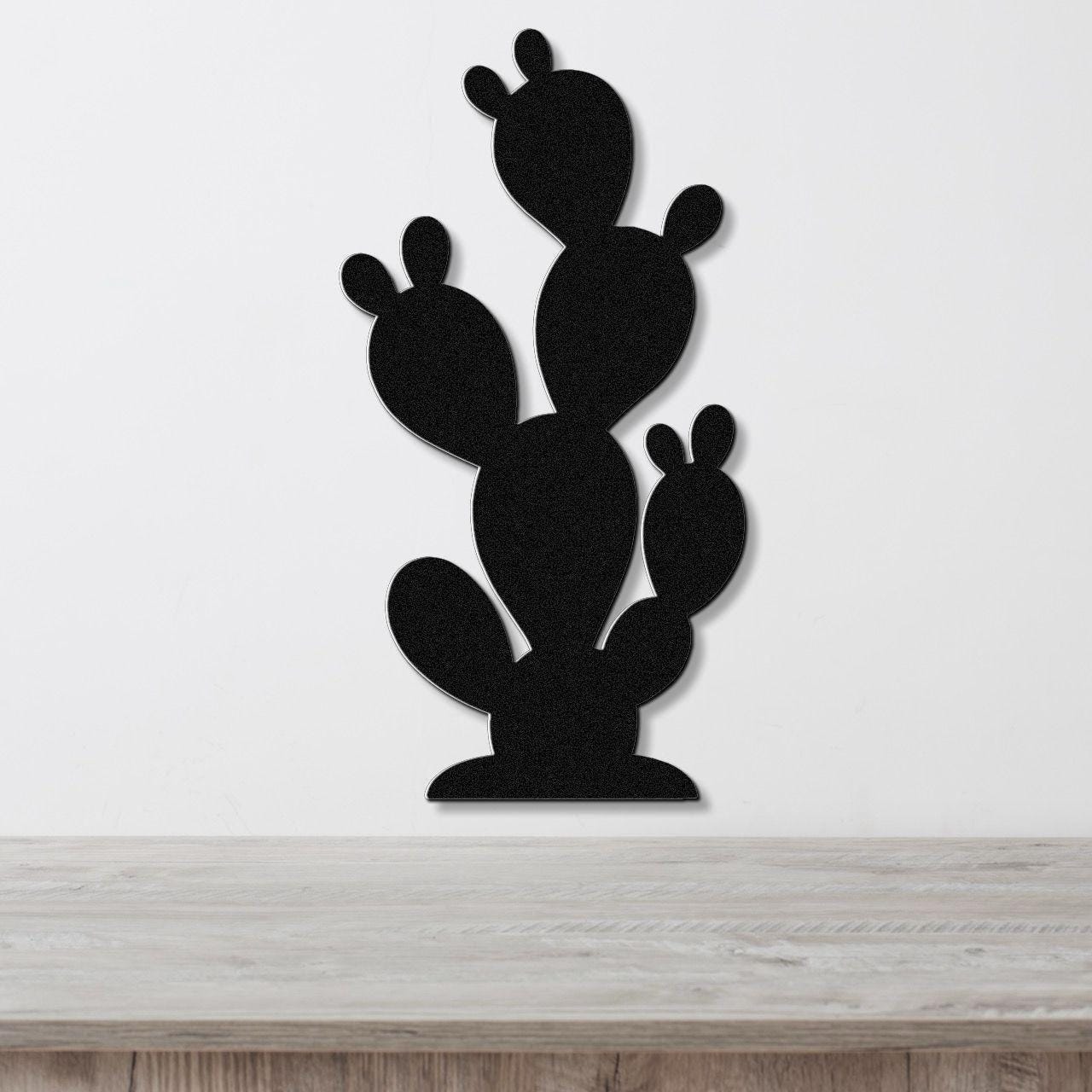 Black metal cactus wall art with layered paddle shapes, mounted on a white wall above a light wood surface.