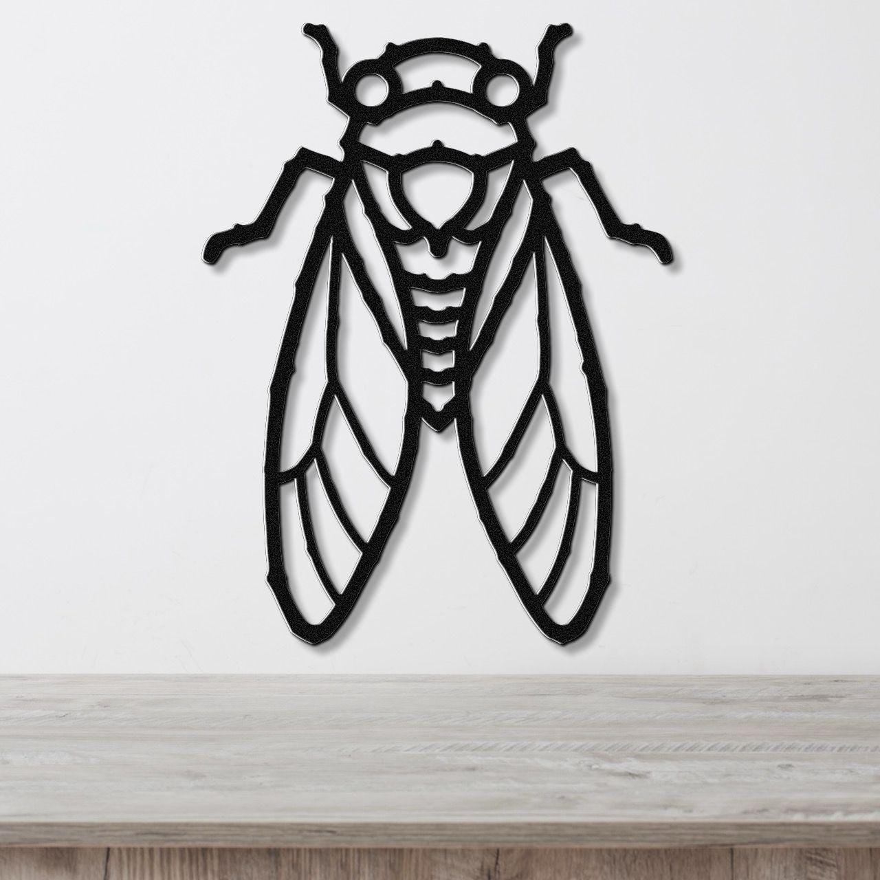 Black metal cicada wall art with detailed wing and body cutouts, mounted on a white wall above a light wood countertop.