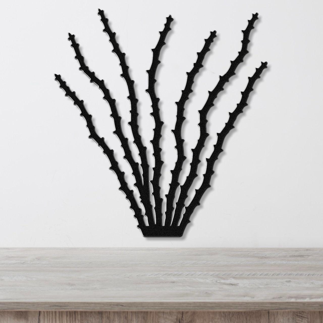 Black metal ocotillo wall art with spiky branch cutouts, mounted on a white wall above a light wood counter.