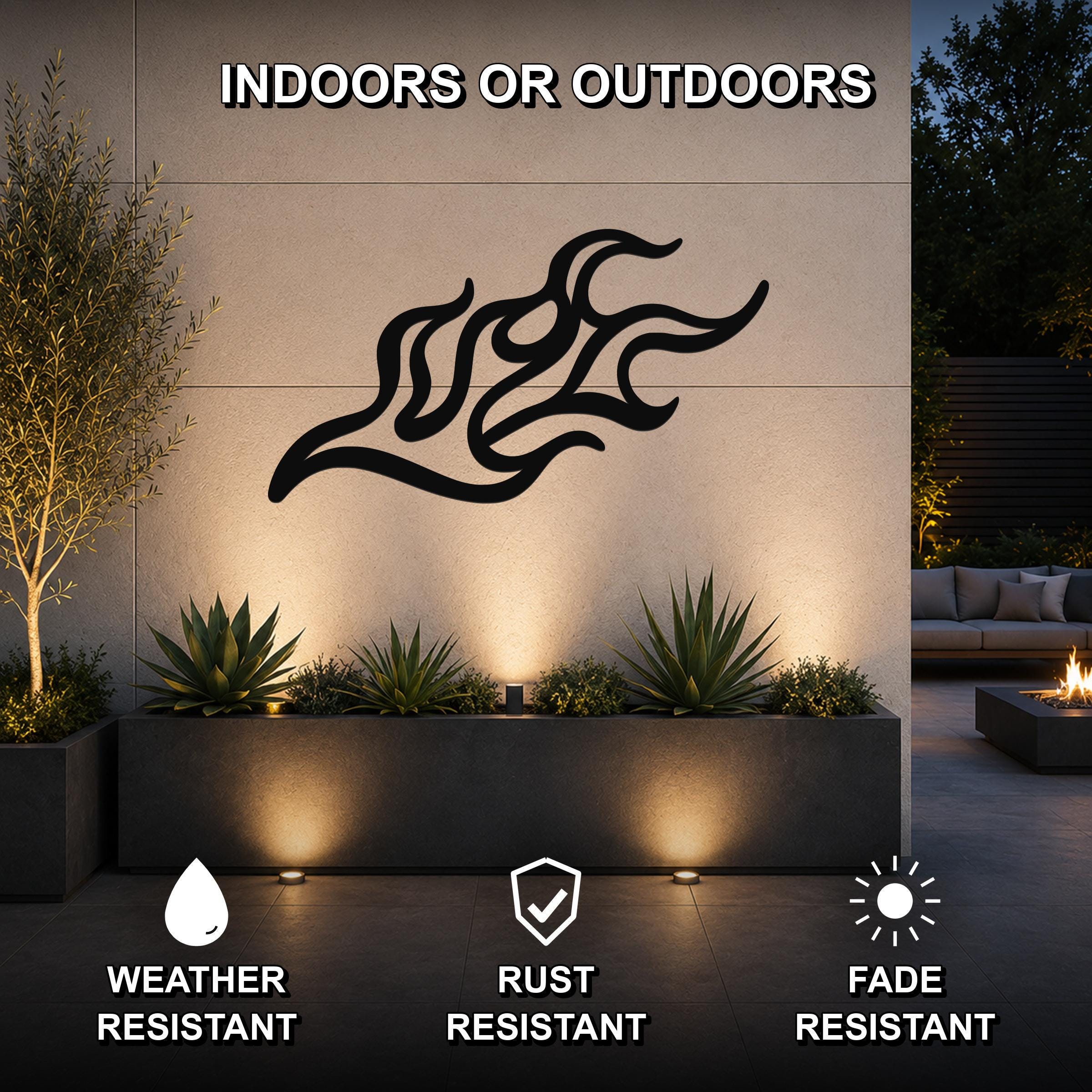 Black metal flame wall art with flowing, abstract cutouts, mounted on an outdoor wall above a planter in a modern patio setting.